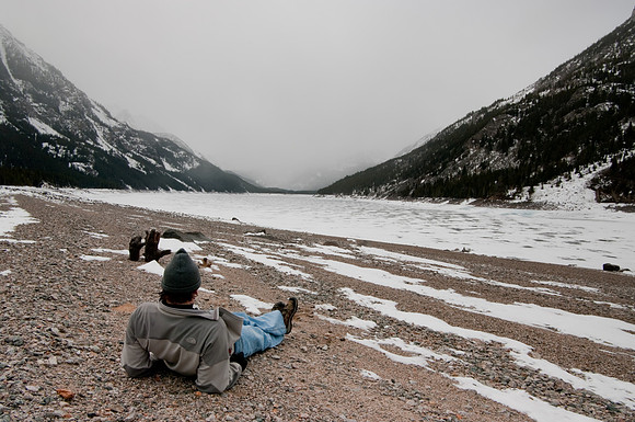 Hiker resting on bank of Mystic lake in winter.
